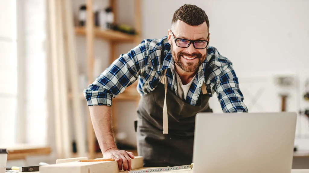 Tischler arbeitet in seiner Werkstatt am Laptop.